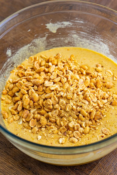 A mixing bowl with peanuts, brown sugar, eggs, flour, corn syrup, and vanilla extract.