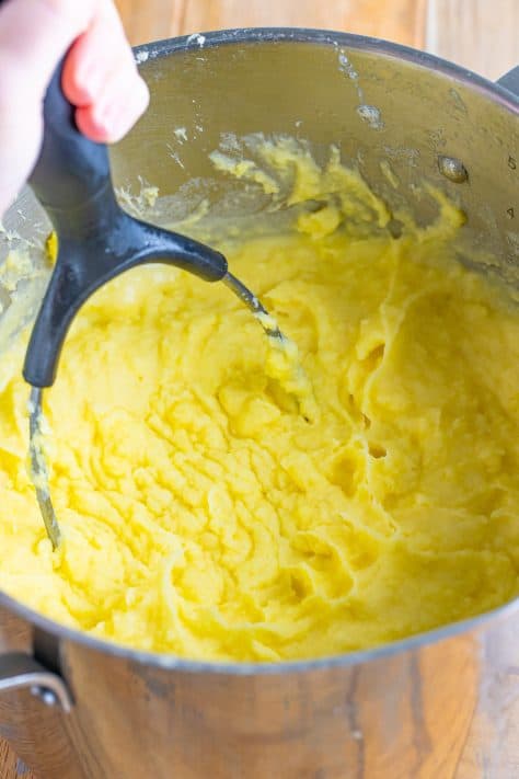 A potato masher mashing potatoes in a pot.