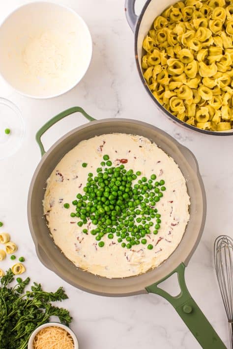 Peas and a cream sauce in a skillet.