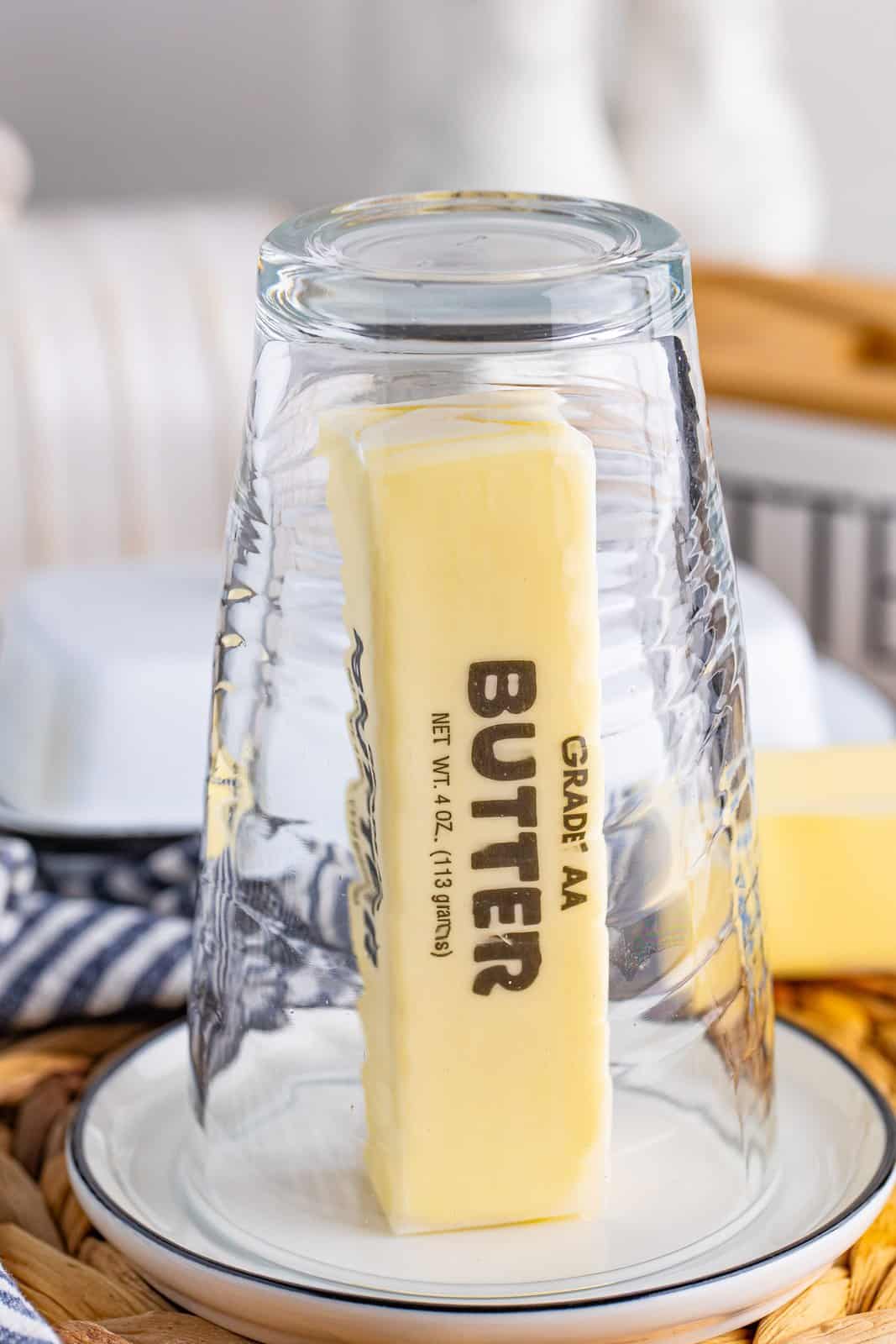 A glass over a stick of butter on a plate.