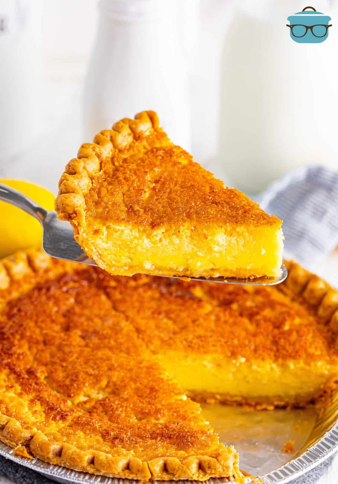 A slice of Buttermilk Pie being held above the rest of the pie.