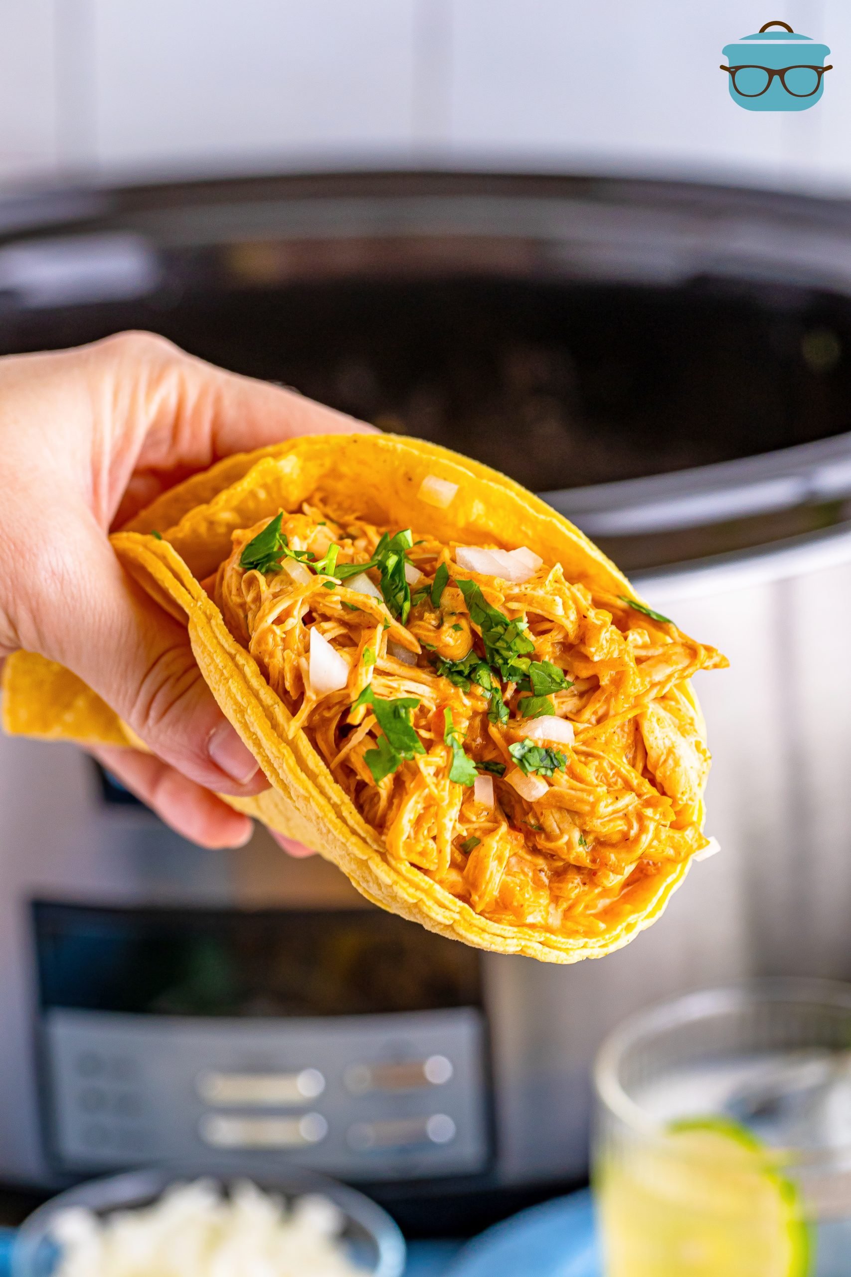 A large Chicken Taco with Shredded Chicken from the slow cooker being held by a hand. 