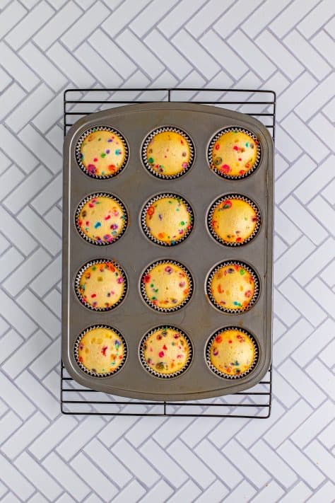 Fresh baked Funfetti Cupcakes still in the cupcake tin sitting on a wire rack cooling.