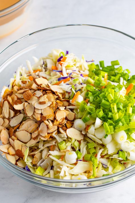 A larger glass mixing bowl with slaw mix, green onions, and almonds.