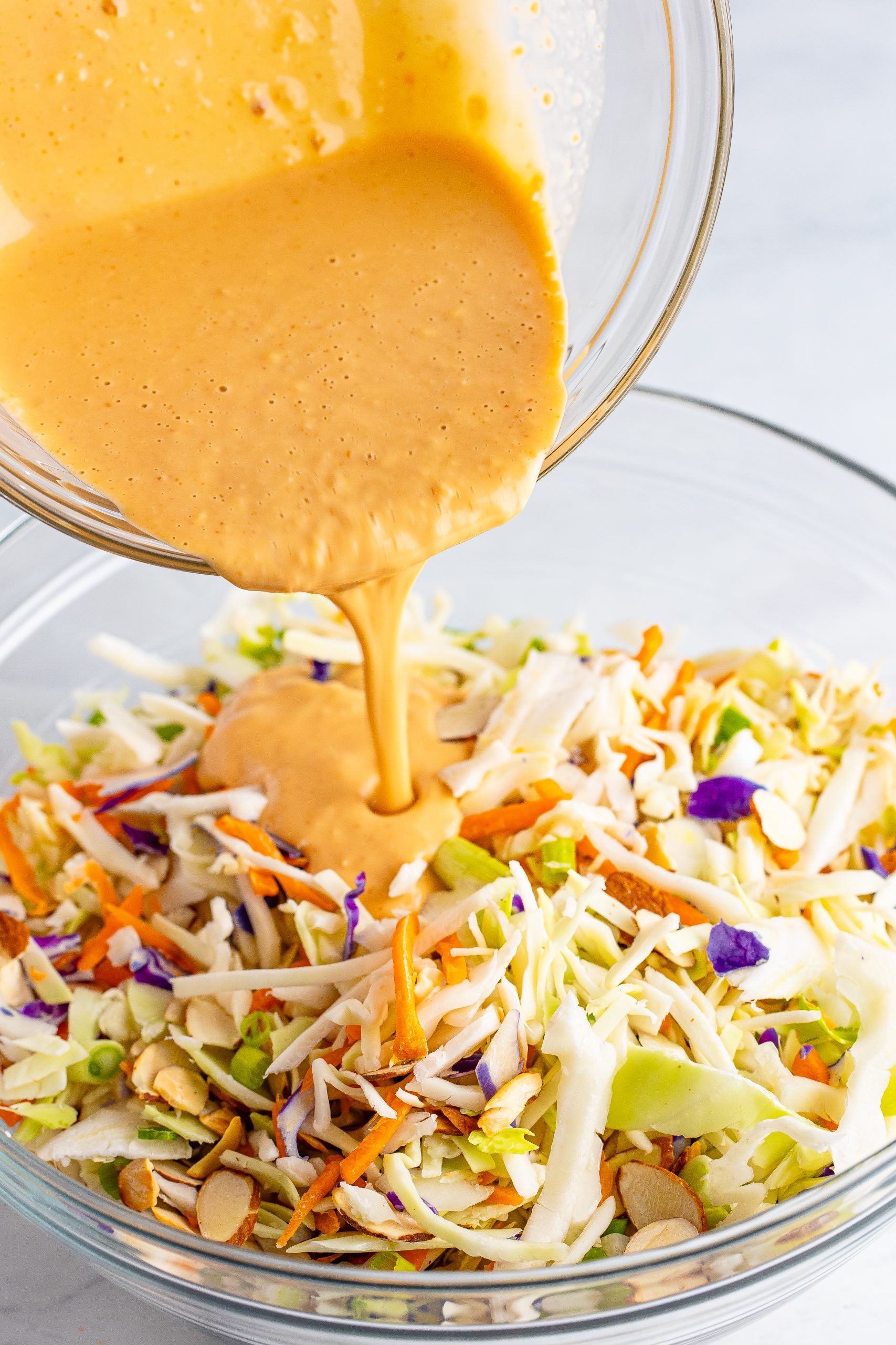 Homemade dressing being poured over the Asian slaw mix. 