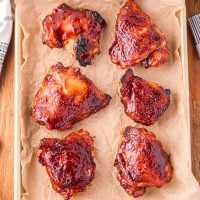 A sheet pan with a few baked chicken thighs covered in bbq sauce.