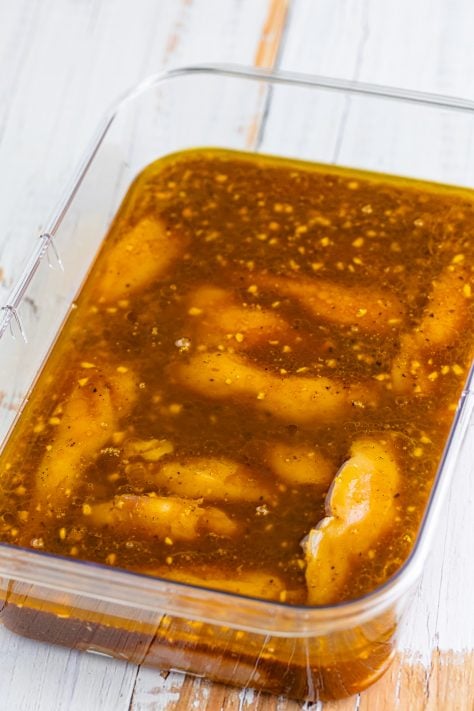 Chicken tenders in marinade in a container.