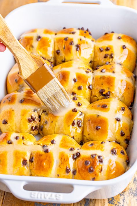 A brush brushing the glaze on fresh baked Hot Cross buns.