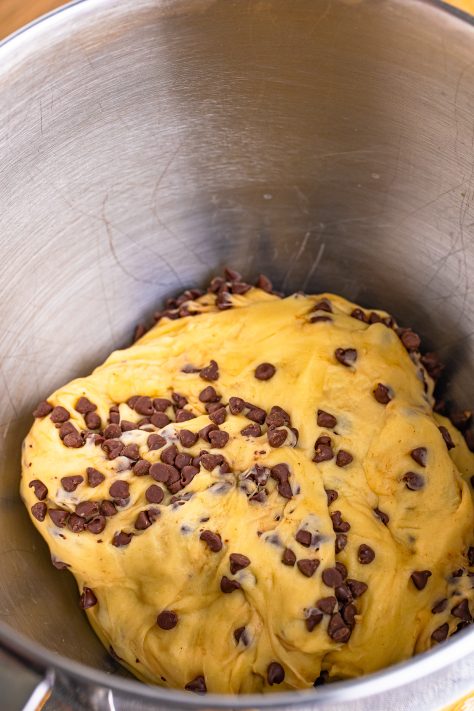 Mini chocolate chips sprinkled in bun dough in a mixing bowl.