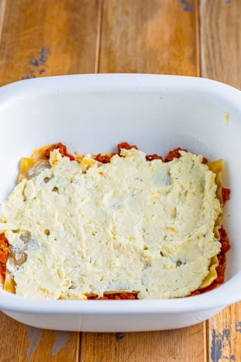 Ricotta cheese mixture on top of noodles and sauce in a baking dish.