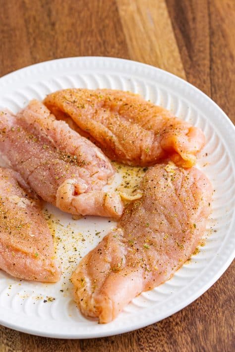 Seasoned raw chicken on a plate.