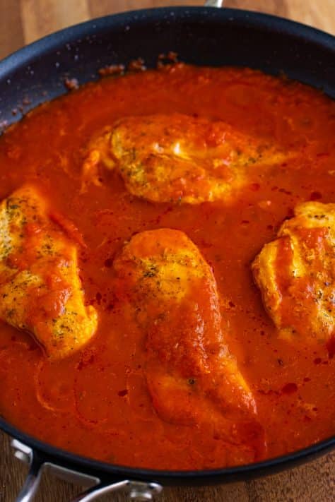 A skillet with marinara sauce and chicken breasts.