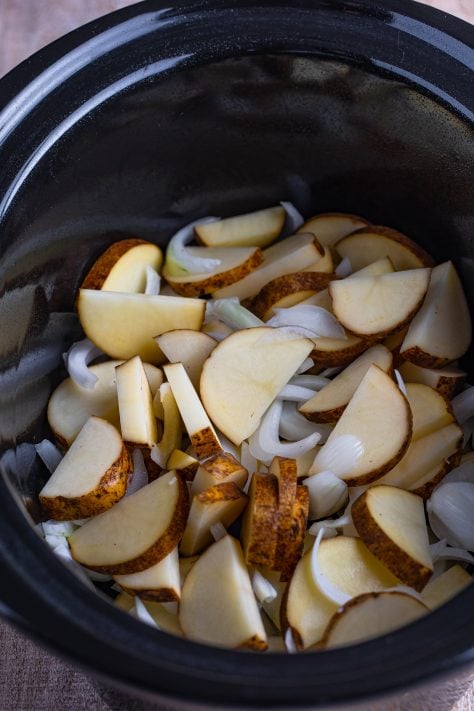 Sliced potatoes and onions in a Crock Pot.