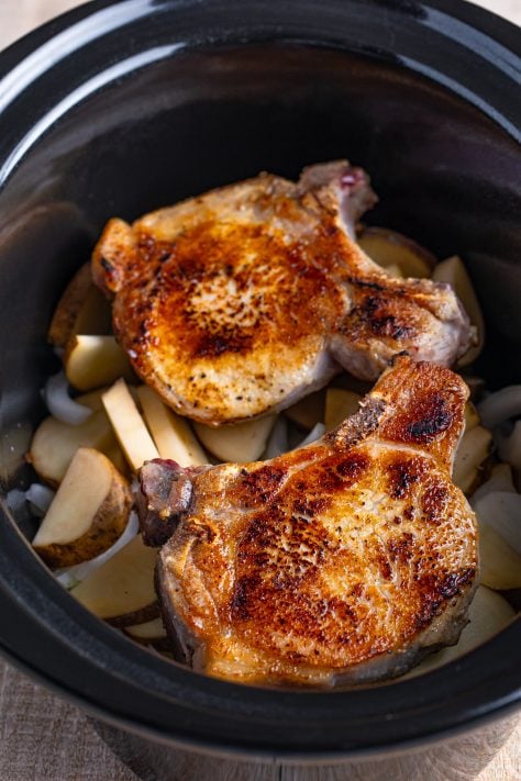 Potatoes, onions, and seared pork chops in a slow cooker.