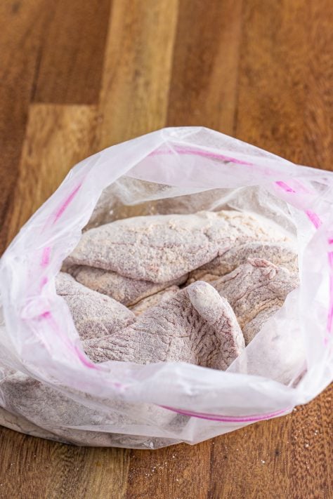 Flour and season covered steaks in a plastic bag.