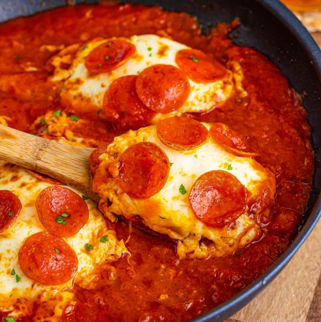 Pepperoni Chicken in a skillet with a wooden spoon holding a serving.