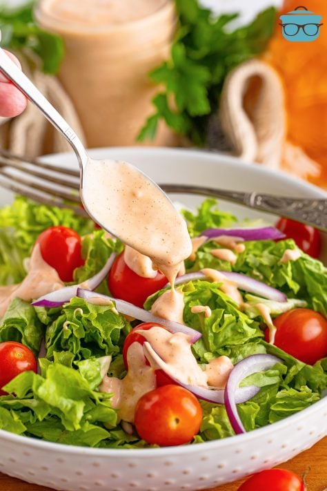A spoon drizzling some Thousand Island Dressing on a salad.