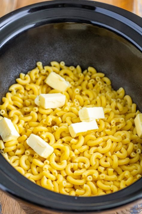 butter slices placed on top of macaroni noodles in crock pot.