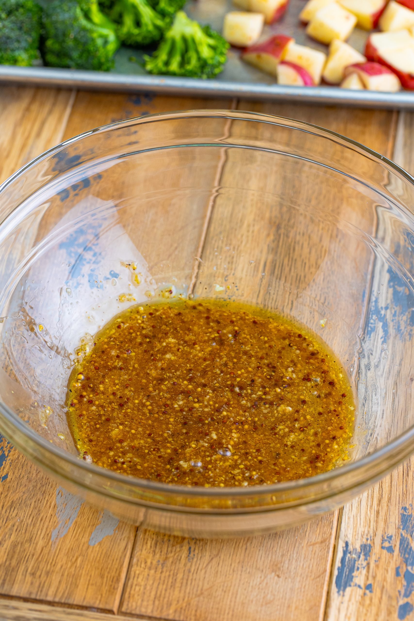 A glass bowl with honey, olive oil, mustard, garlic, and creole seasoning.