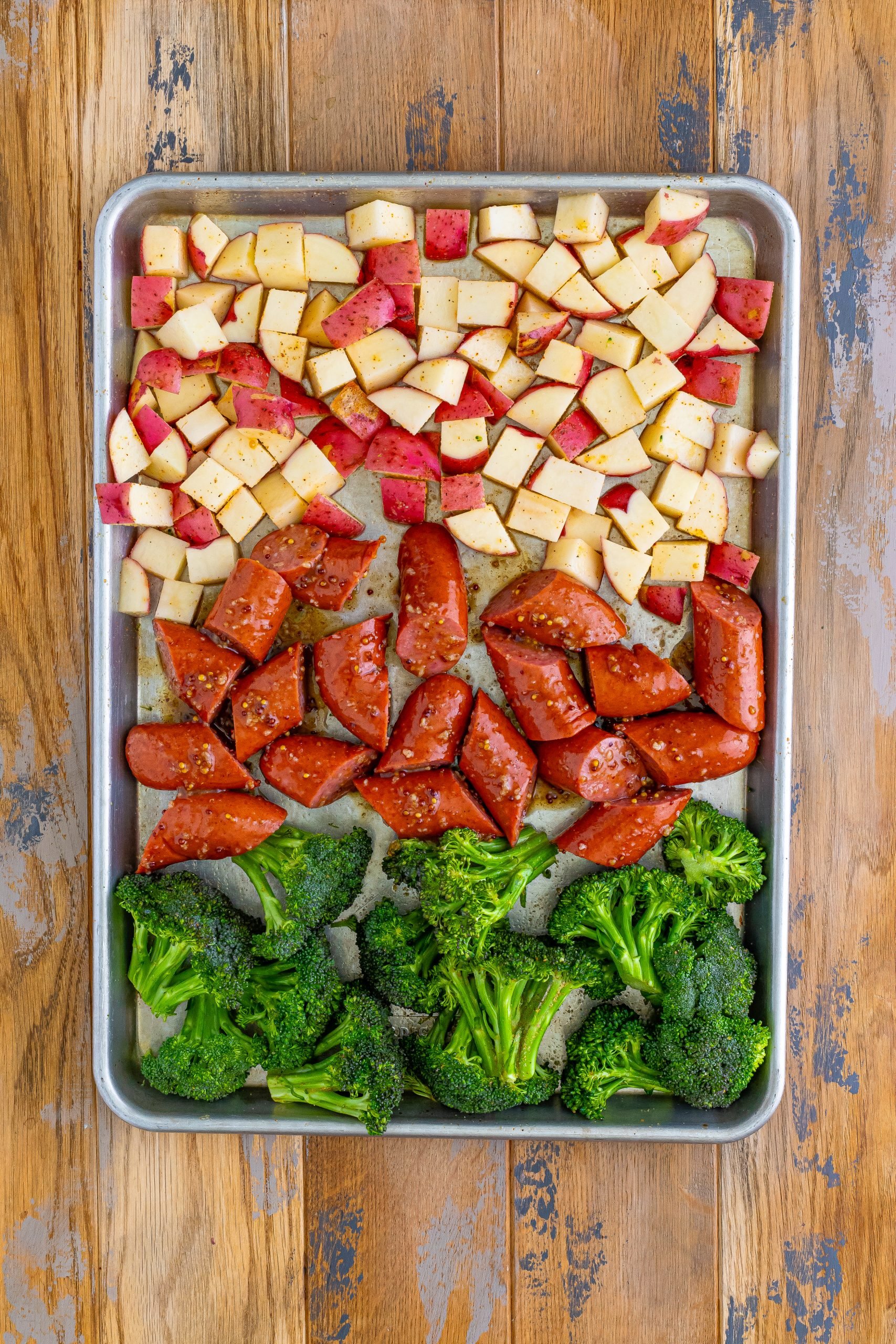 Kielbasa coated with sauce, broccolini, and potatoes on a sheet pan.