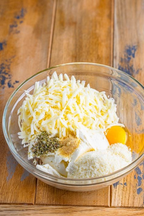 ricotta cheese, egg, parmesan cheese, mozzarella cheese, Italian seasoning, garlic powder in a bowl.