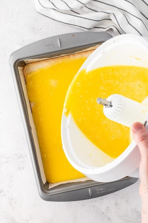 Lemon mixture being poured on crust in a baking dish.