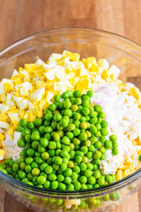 chopped boiled eggs, and frozen peas added into bowl with macaroni.