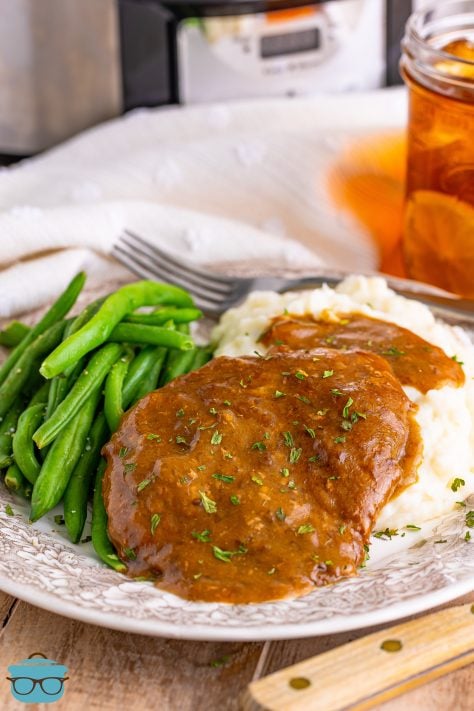 cube steaks covered with gravy on a plate with green beans and mashed potatoes.