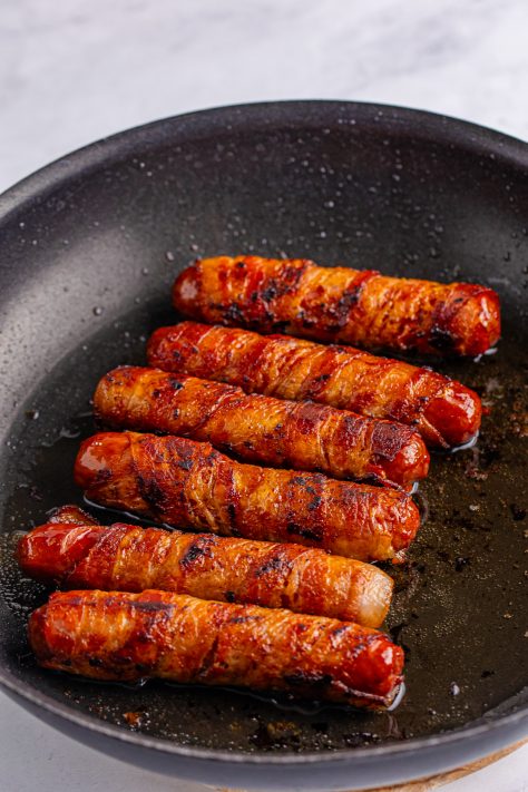 cooked bacon wrapped bratwurst in a pan.