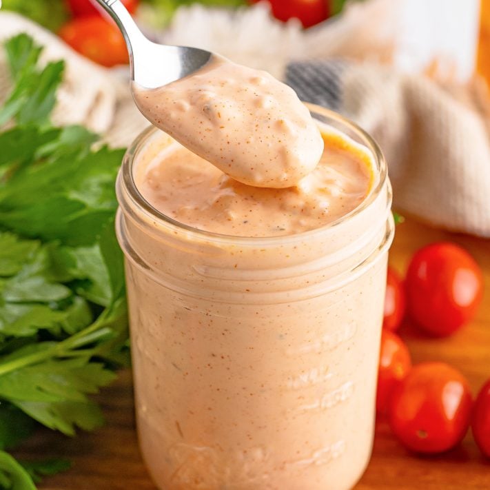A spoon getting some homemade Thousand Island Dressing from a jar.
