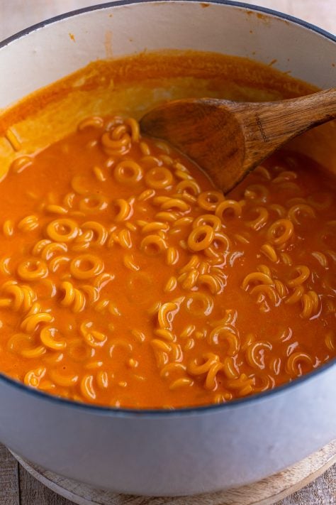 spaghettios simmering in a pot with tomato sauce and a wooden spoon.