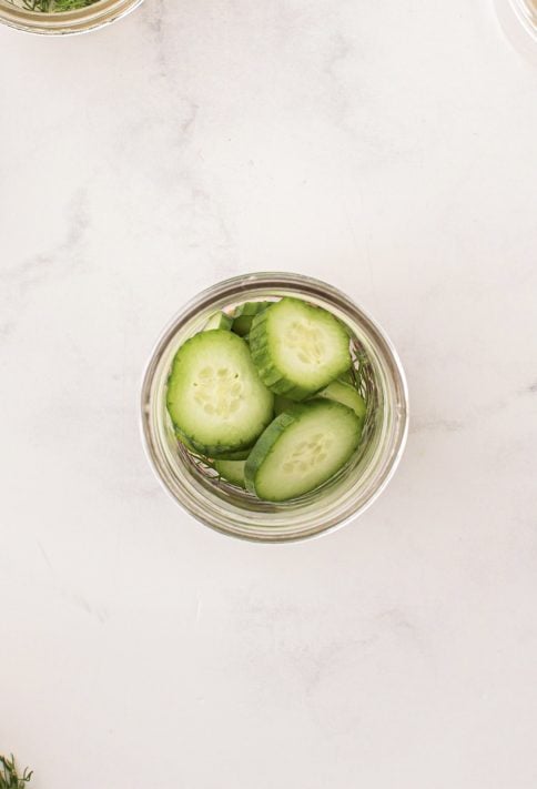 sliced cucumbers are added to mason jar.