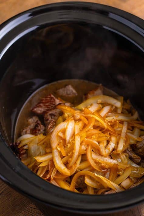cooked onions added to slow cooker with beef stew meat.
