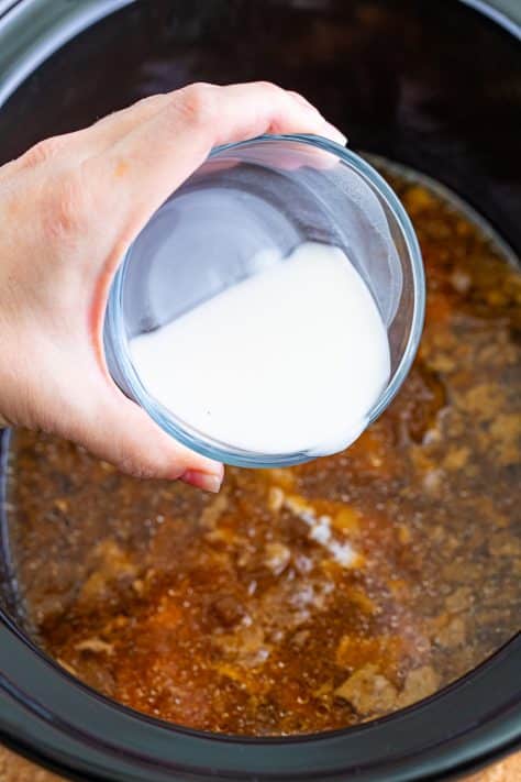 Cornstarch slurry being poured in the Crock Pot with the pork chops.