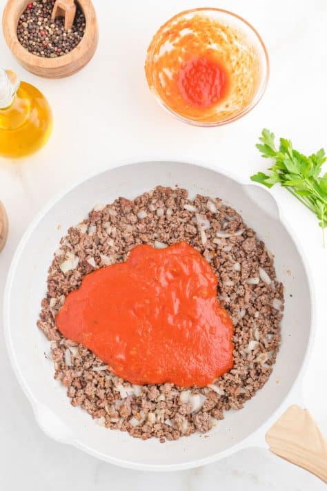 Ground beef, onion, and tomato sauce in a skillet.