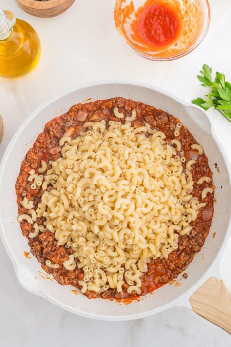 Macaroni pasta, tomato sauce, ground beef, and onion in a skillet.