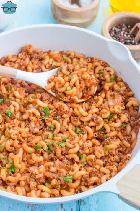 A wooden spoon in a skillet of Beefaroni.