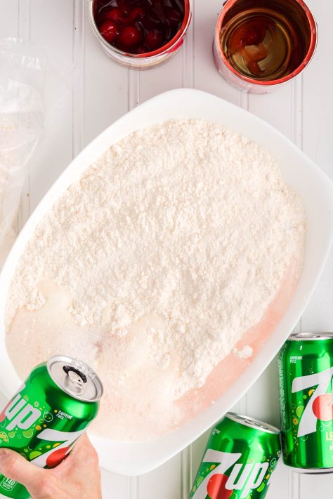 7Up being poured over cake mix and cherry pie filling.