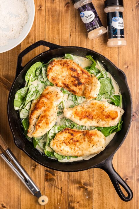 Chicken in a sauce with spinach in a skillet.