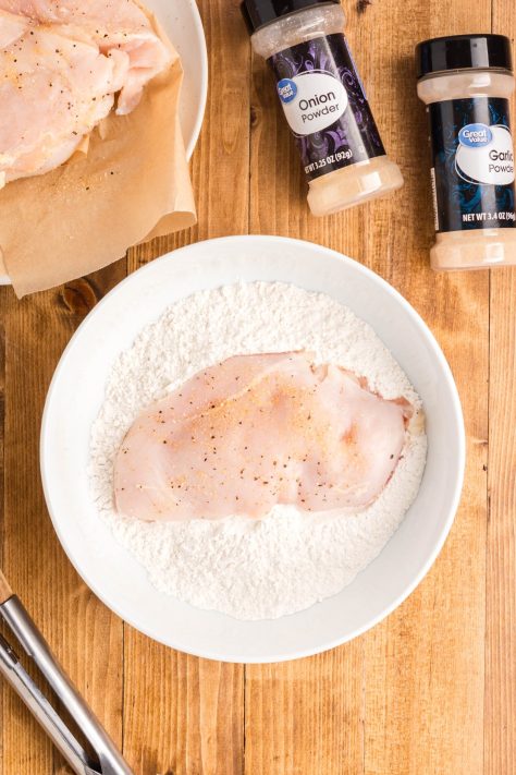 Chicken being dipped in a flour mixture.