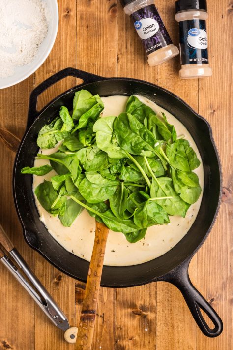 Spinach being added to a cream sauce in a skillet.