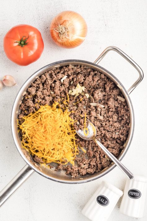 Shredded cheese and garlic being added to a ground beef skillet.