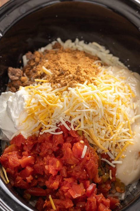 A slow cooker with potatoes, beef, seasoning, sour cream, cheddar soup, Rotel and 1 ½ cups Colby Jack shredded cheese.
