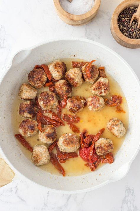 Meatballs, sun dried tomatoes and broth in a skillet.
