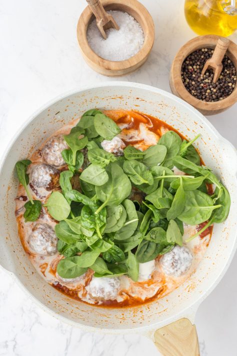 Cream and spinach being added to the meatball mixture.