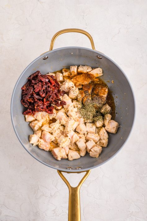 Ingredients being added to the chicken in a skillet.