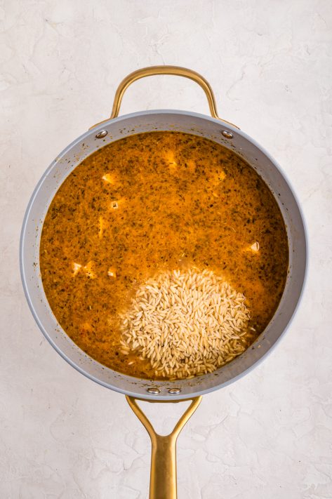 Broth and orzo being added to a skillet.