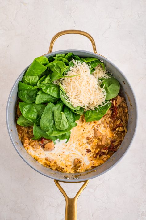 Spinach and cheese being added to a skillet.