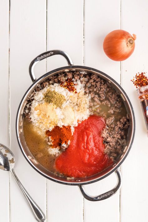 A pan with beef, onions, broth, rice, tomato sauce, and seasonings.