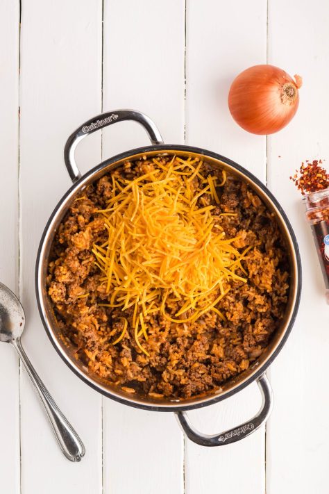 Cheese being added to a dinner in a pan.